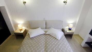 Una cama bien hecha con cubrecama acolchado, dos lámparas de noche y una lámpara fijada a la pared.