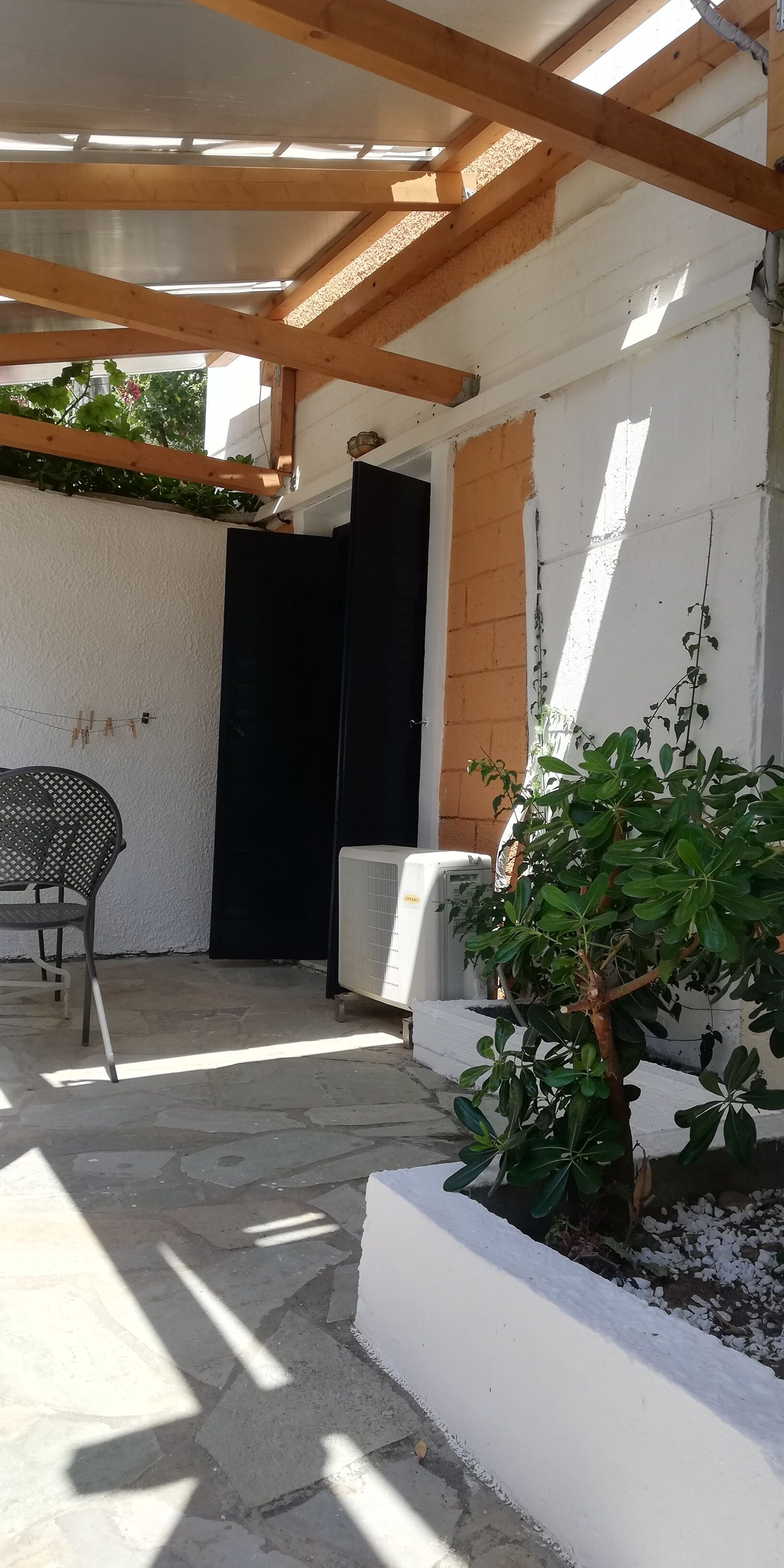 Un'area patio coperta con soffitto in legno, una porta nera, un muro bianco e una pianta in vaso.