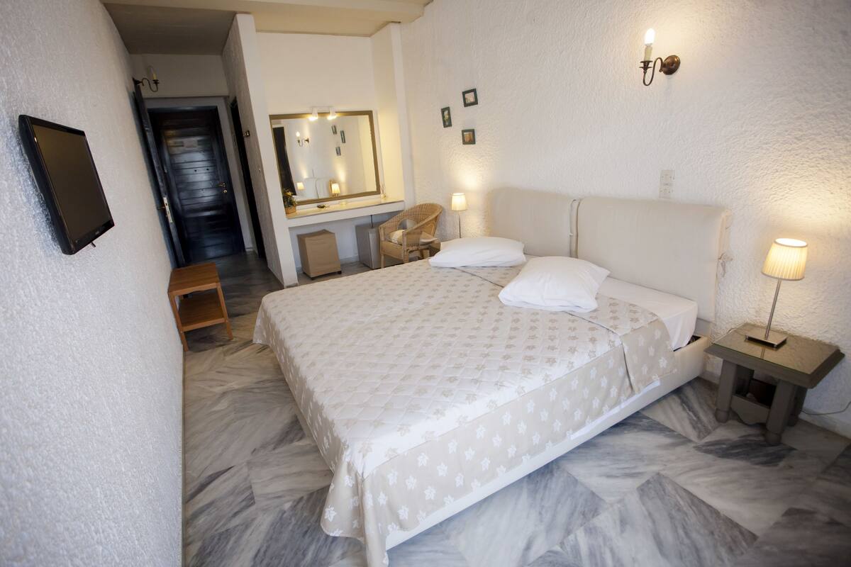 Een hotelkamer met een bed, nachtkastje, lamp, stoel en een spiegel.