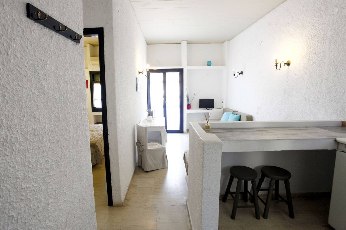 Een compacte keuken met een centraal eiland, twee krukken en een kleine tafel met een vaas.