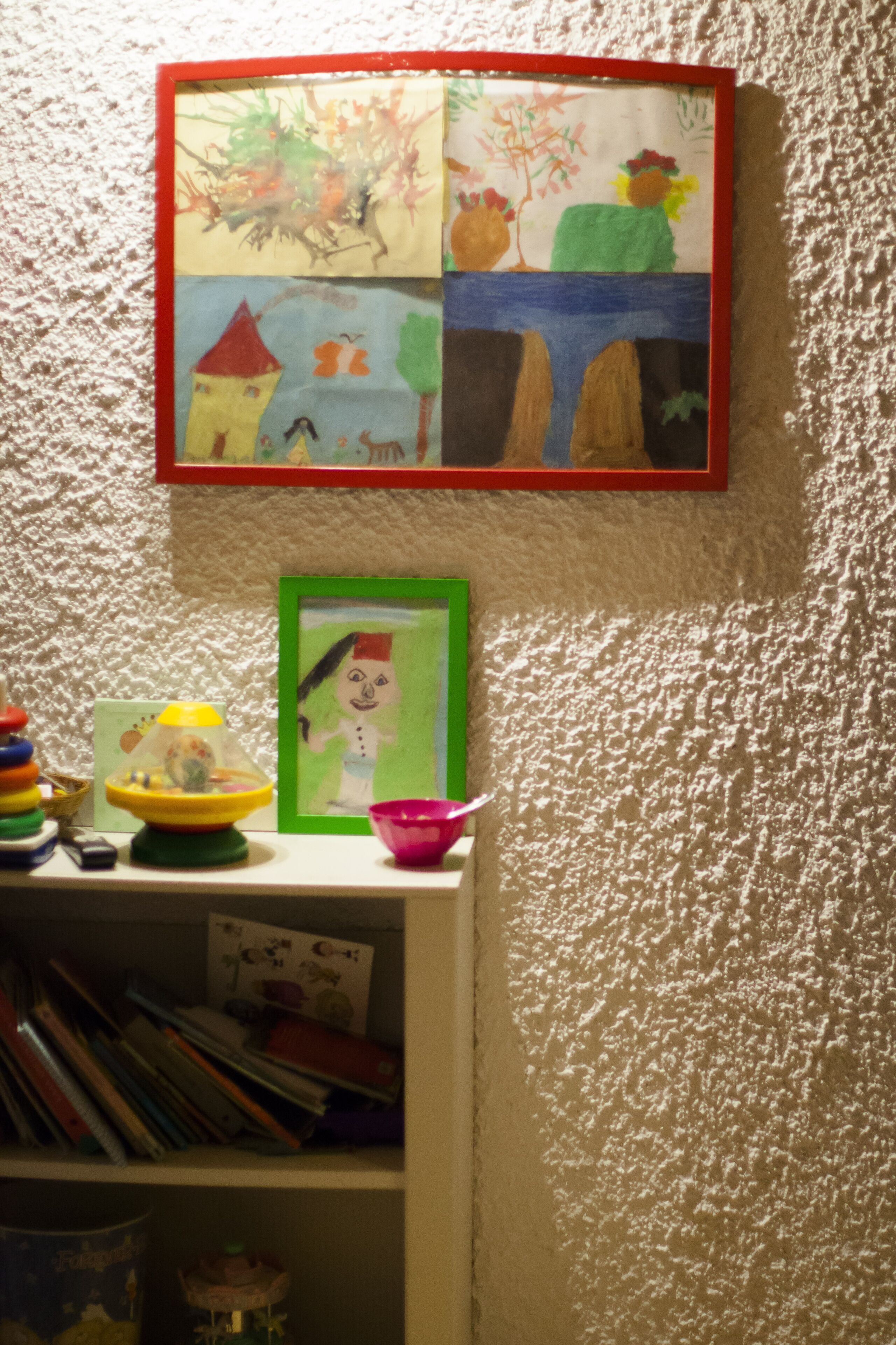 Una pared con un cuadro enmarcado, un estante con libros y un juguete, y una pared con textura.