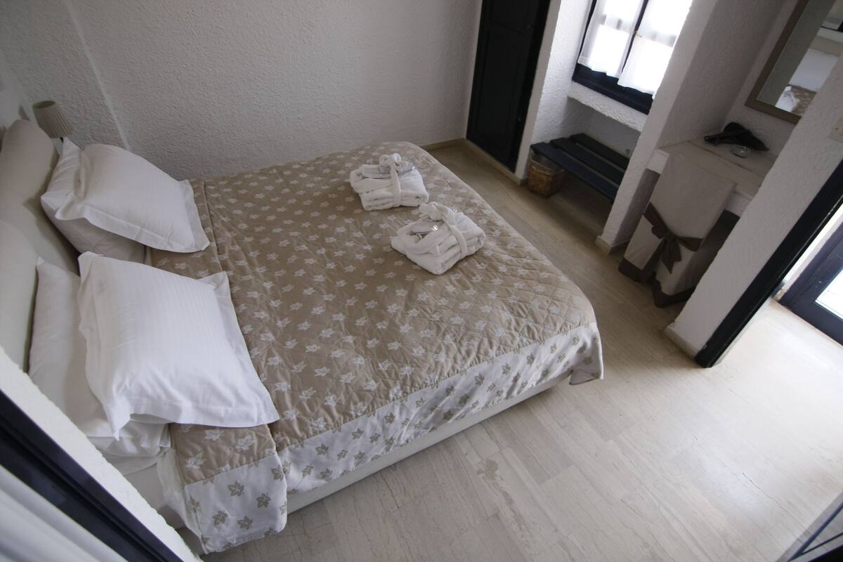 Een net opgemaakt bed met een bloemenprintdeken, twee kussens en twee opgevouwen handdoeken.