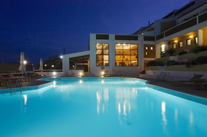 Piscina com espreguiçadeiras e um edifício com grandes janelas ao fundo.