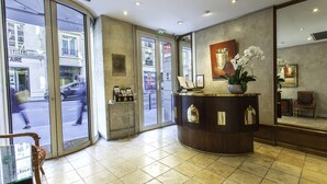 Un espace d’accueil d’hôtel avec un comptoir d’accueil incurvé, une orchidée en pot et un fauteuil.