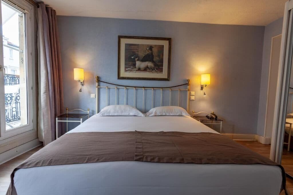 Een hotelkamer met een bed, twee bedlampen, een schilderij aan de muur en een raam met gordijnen.