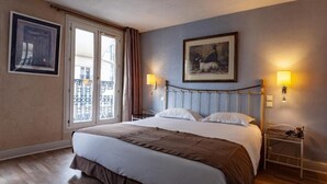 Une chambre d’hôtel avec un grand lit, un balcon avec vue et deux lampes fixées au mur.