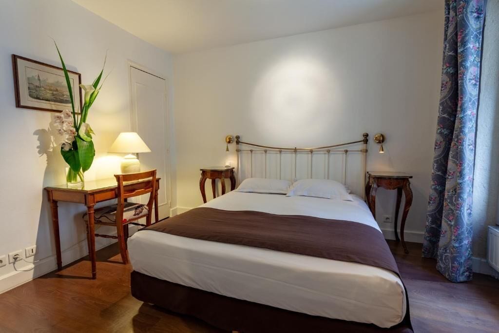 Un dormitorio ordenado con cama, mesitas de noche, un escritorio y una silla.