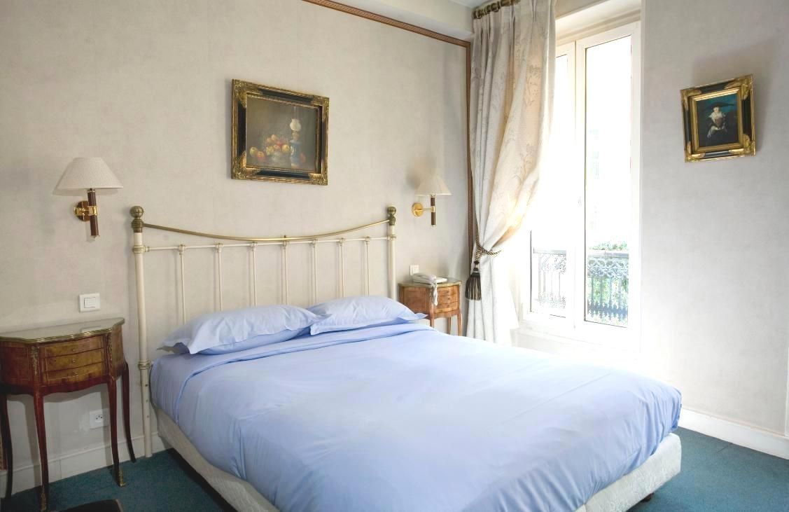 A bedroom with a single bed, two bedside tables, a window with curtains, and two wall-mounted lamps.