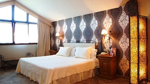 Habitación de hotel con una cama grande, dos mesitas de noche, un banco y una ventana con cortinas.
