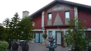 Un edificio de dos pisos con una chimenea de piedra, un ventanal grande y una puerta con un letrero.