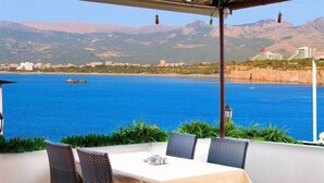 Una mesa con sillas dispuestas al aire libre, con vista a un cuerpo de agua con barcos y edificios al fondo.