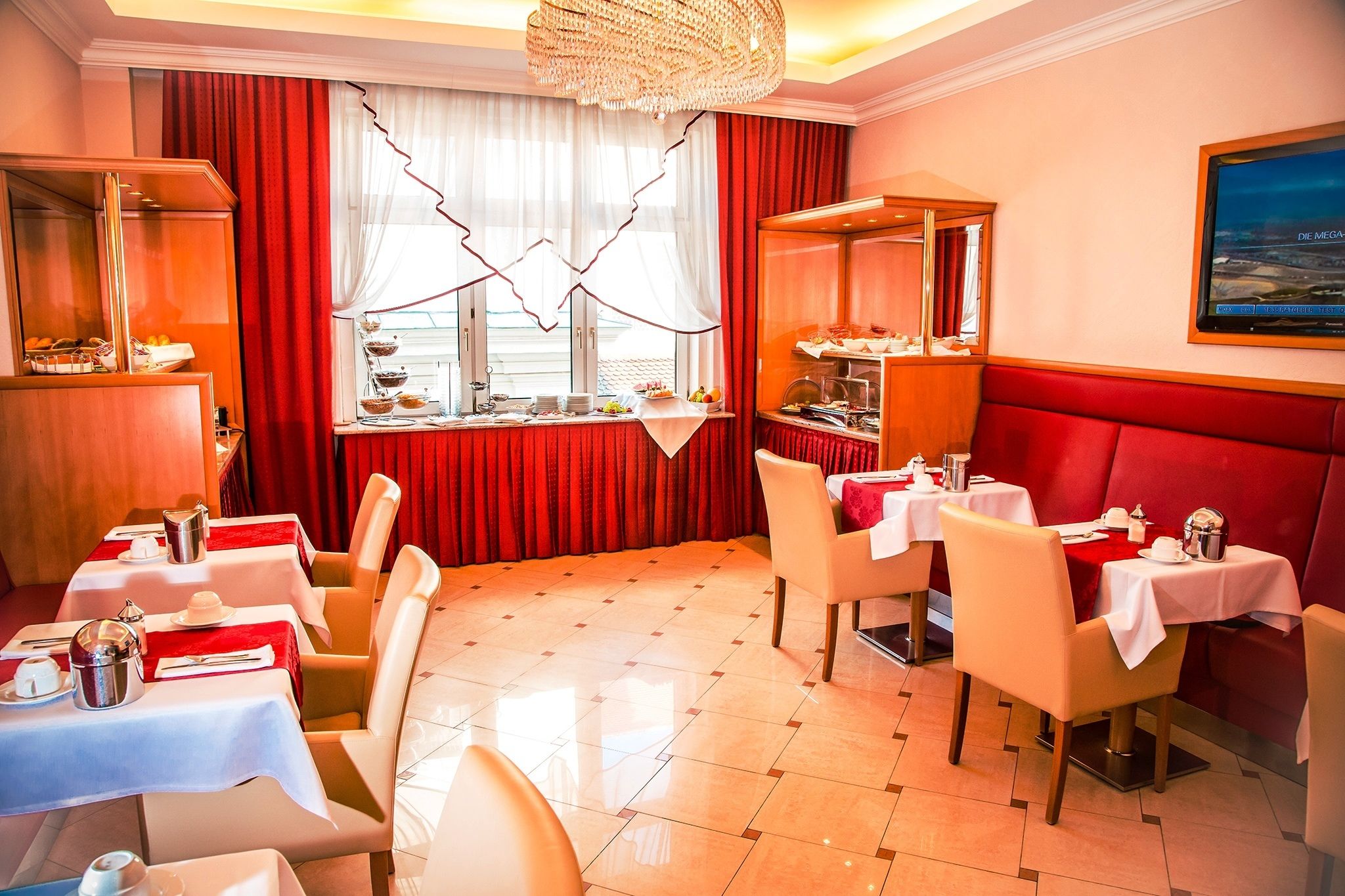 A restaurant with red curtains, white tables, and a chandelier.