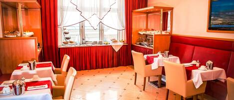 Un restaurant avec des rideaux rouges, des tables blanches et un lustre.