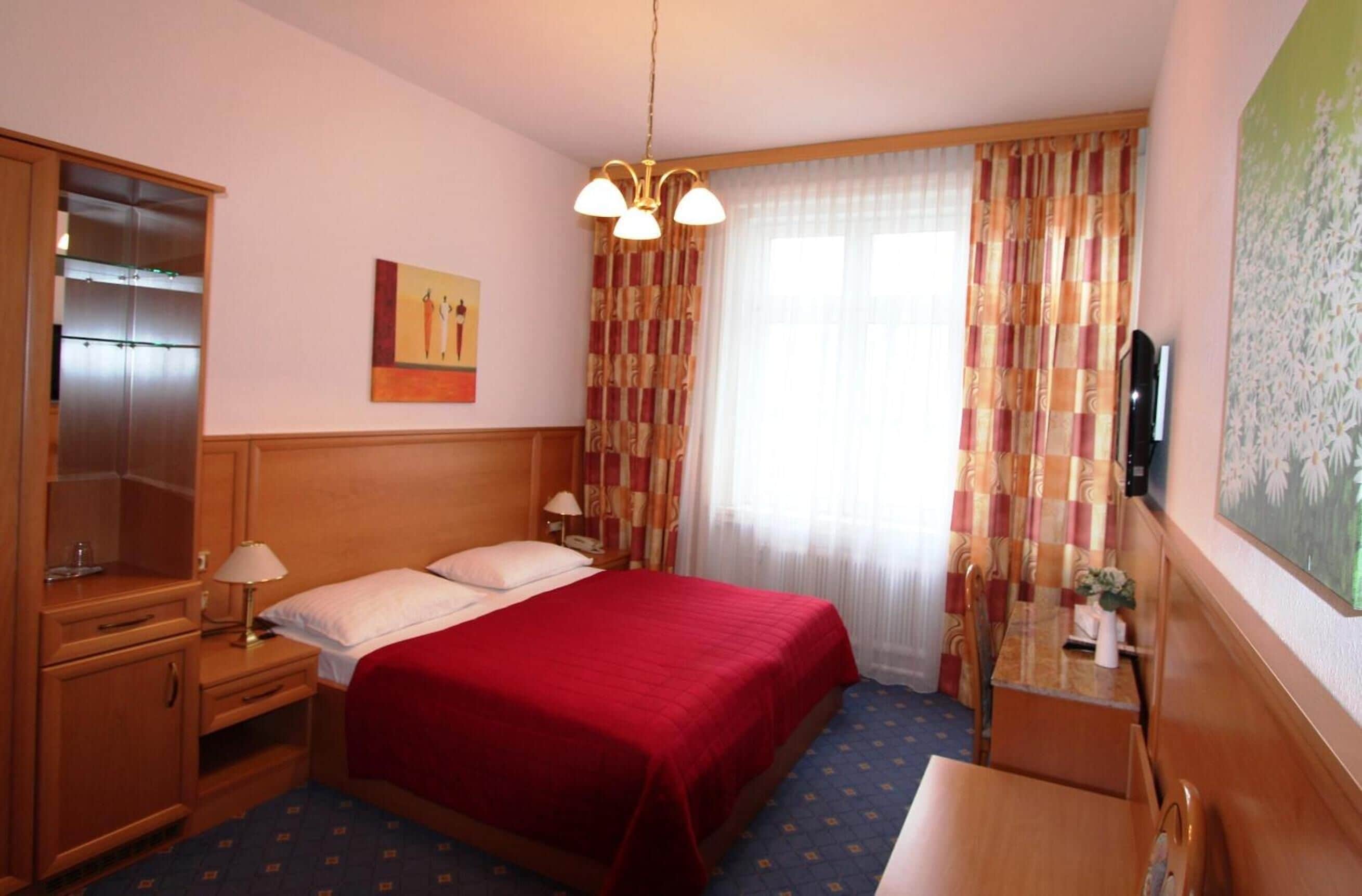 A hotel room with a bed, bedside tables, a desk, a chair, a television, and a window with curtains.