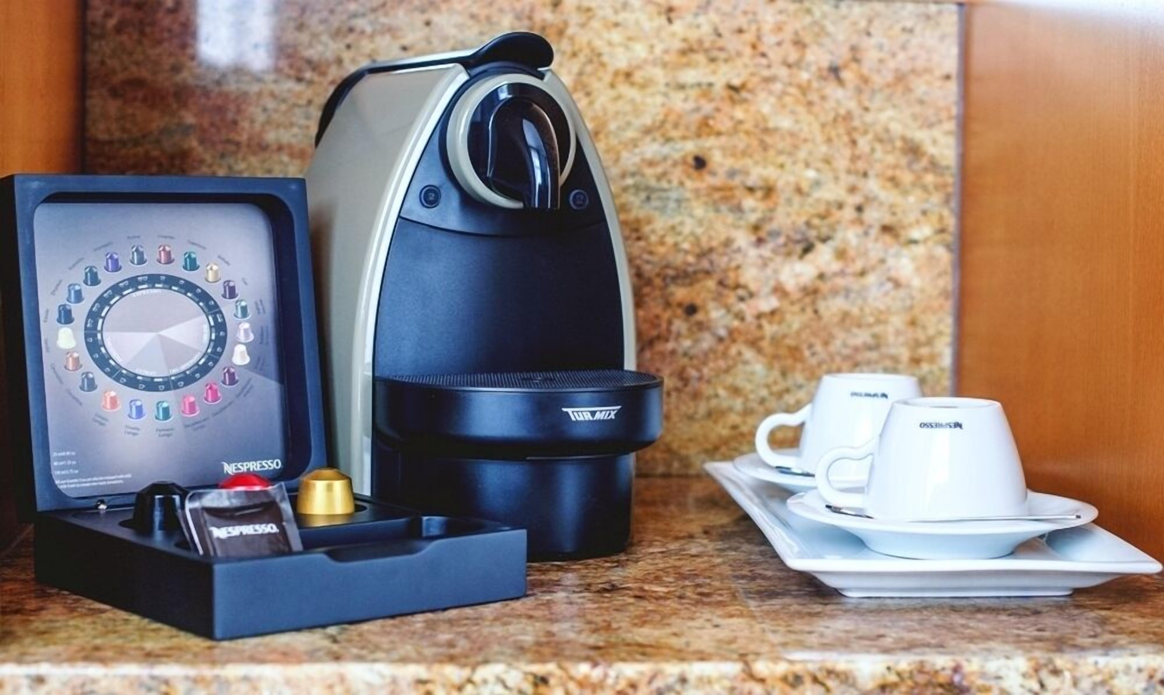 Máquina de café com porta-cápsulas, duas chávenas brancas e um tabuleiro.