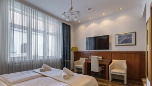 A hotel room with a large bed, a desk with chairs, a TV, and a painting on the wall. - Hotel Corvinus (Vienna)