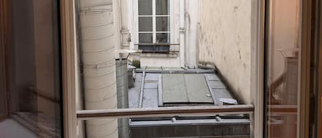 Vista desde una ventana estrecha hacia el interior de un edificio, que incluye una ventana con una reja metálica y un ventanal pequeño con cortina.
