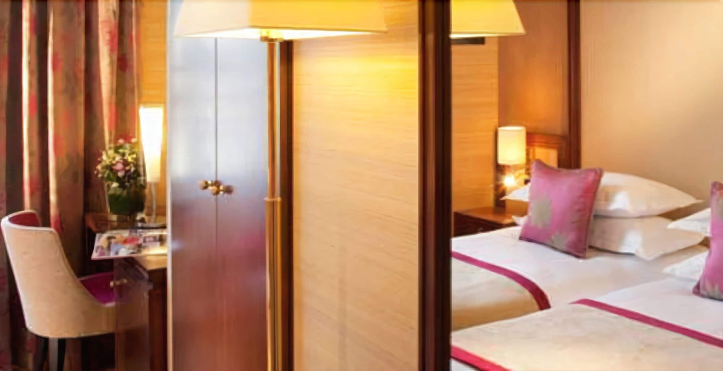 Una habitación de hotel con cama, escritorio, silla y mesita de noche con lámpara.