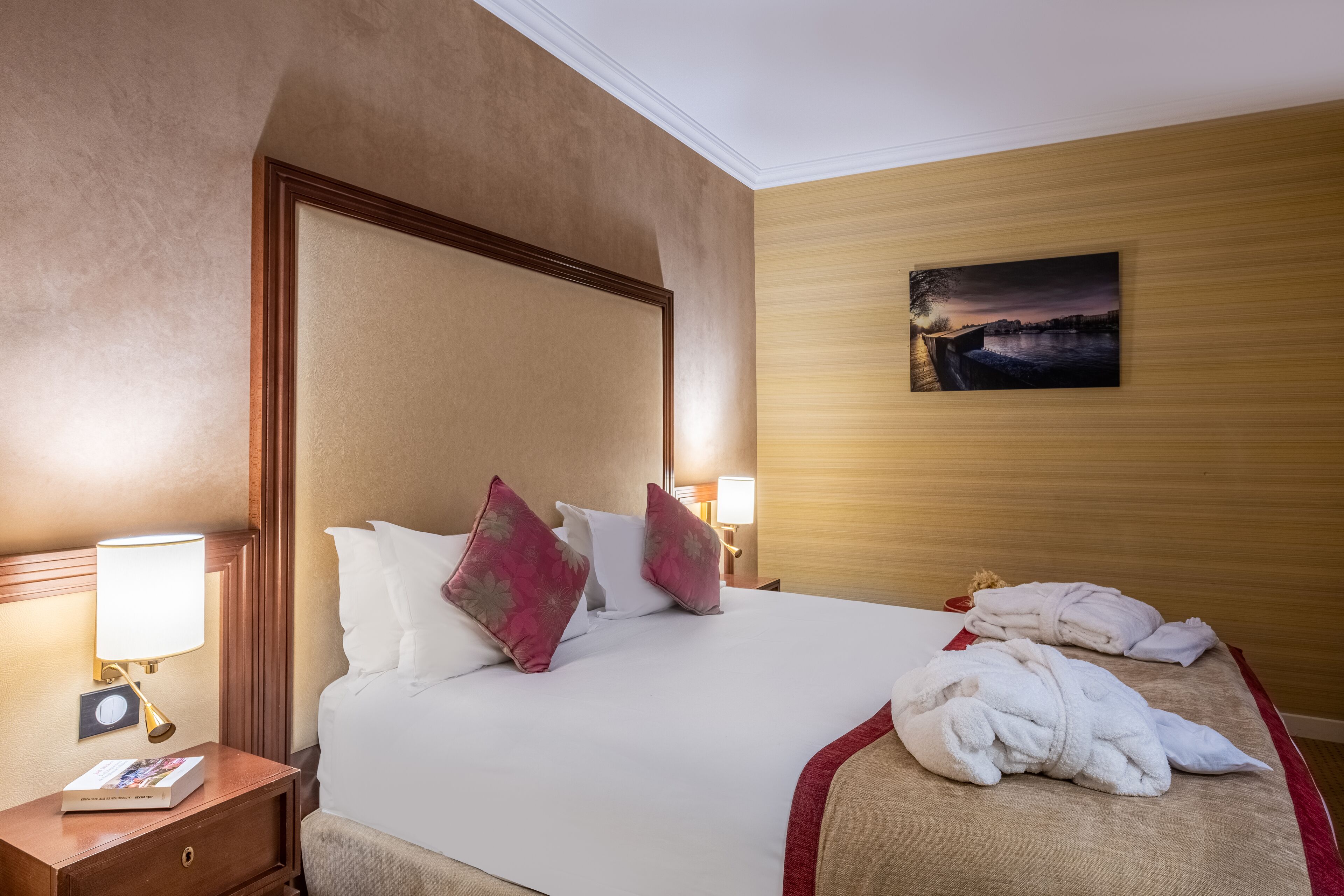 Une chambre d’hôtel avec un grand lit, deux lampes de chevet, une table de chevet avec un livre et un tableau au mur.