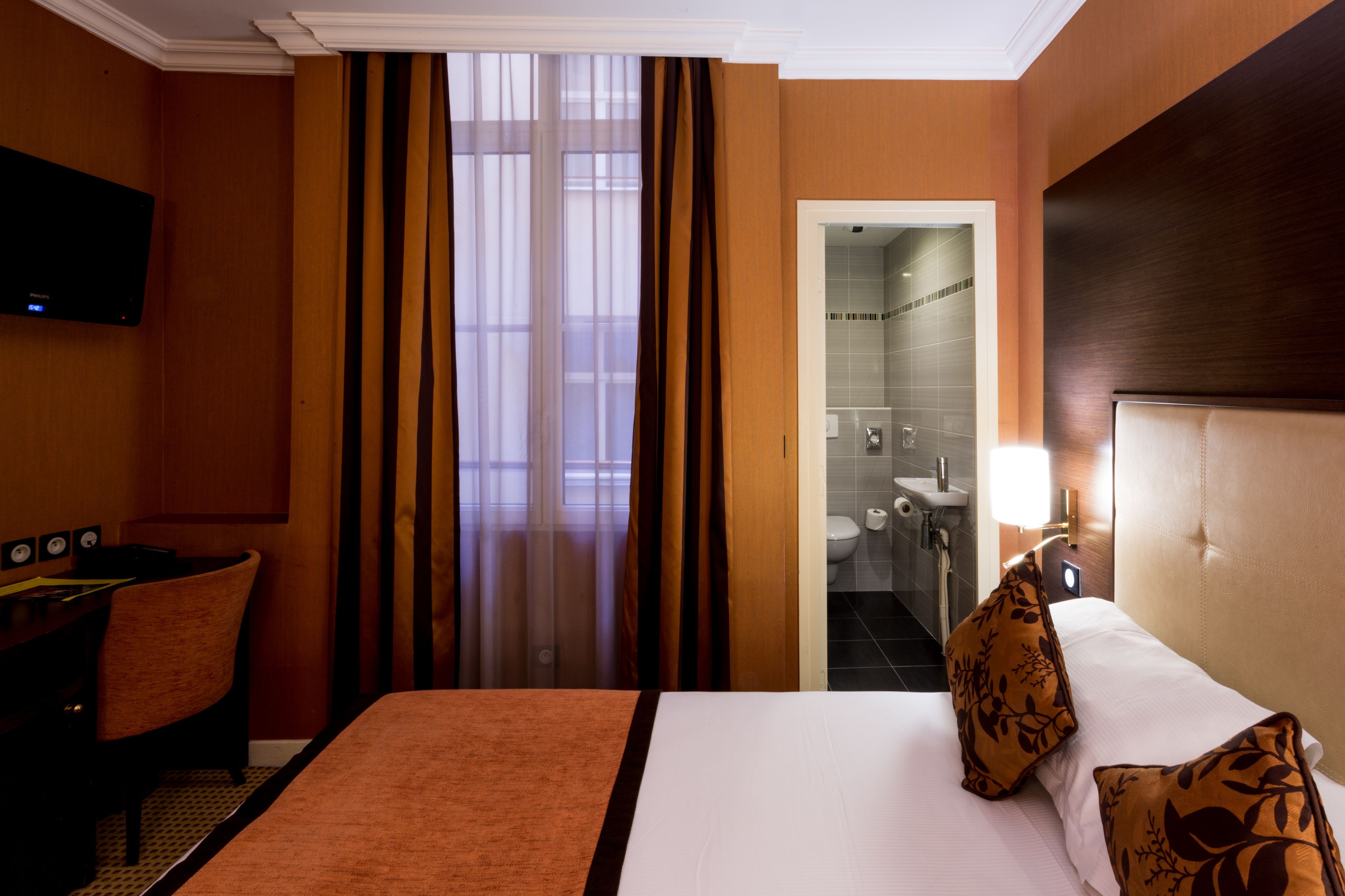 A hotel room with a bed, a desk, a chair, and a TV.