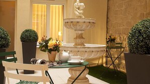 A courtyard with a fountain, a table with a teapot and cups, and potted plants. - Hotel Saint Honore 85 (Paris)
