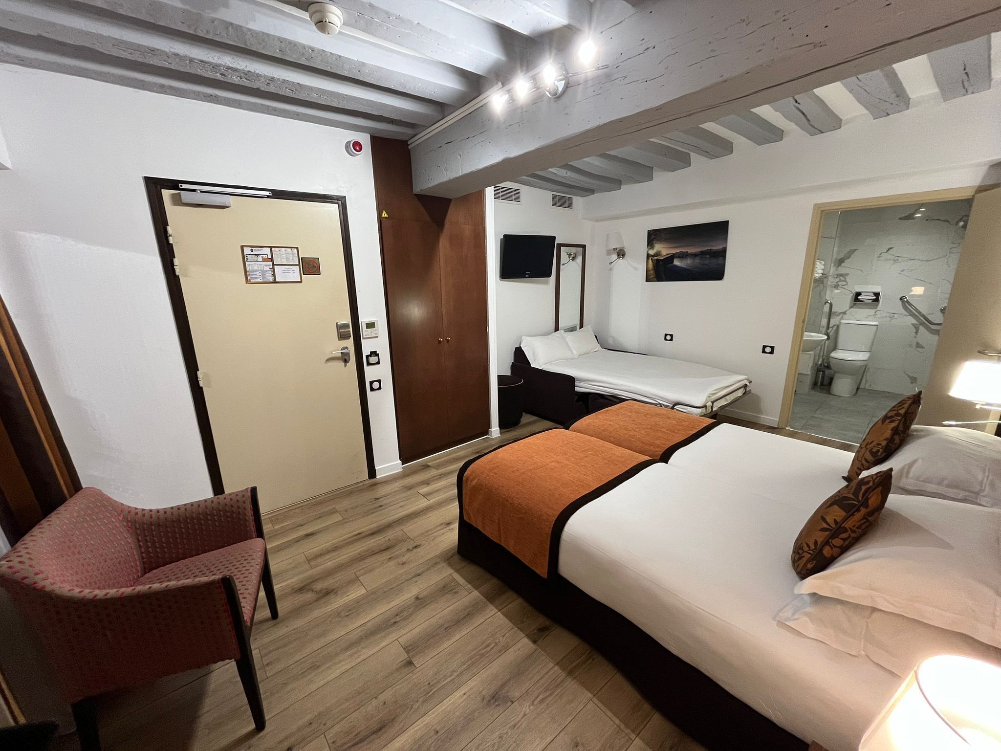 A hotel room with a bed, a chair, a desk, a mirror, and a bathroom visible through an open door.