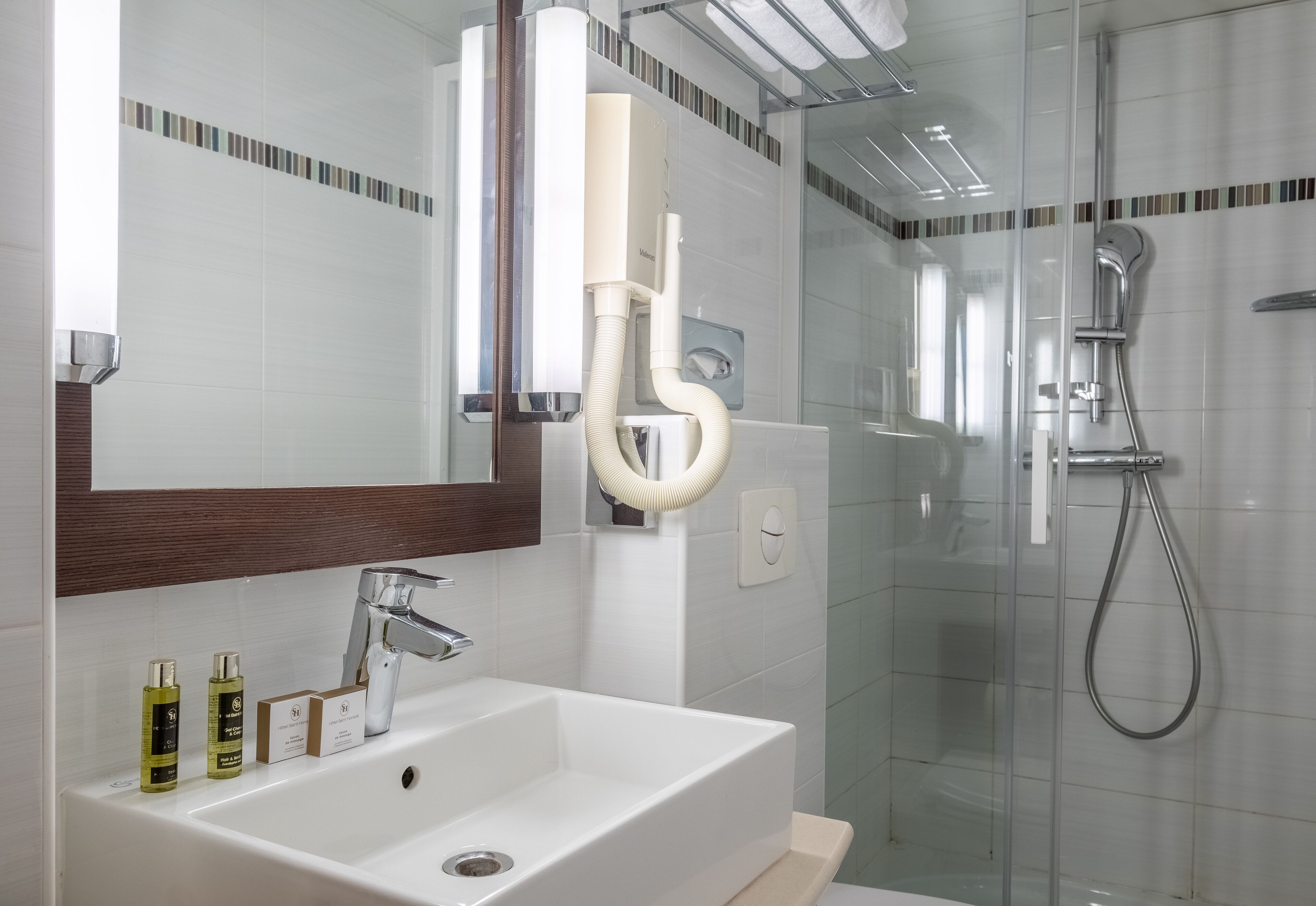 Un baño moderno con lavamanos blanco, espejo y cabina de ducha de vidrio.