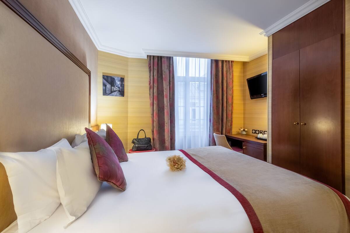 A hotel room with a large bed, a desk, a TV, and a wardrobe.
