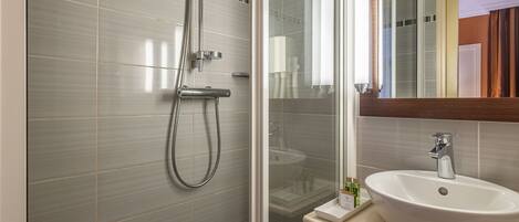 A modern bathroom with a glass shower enclosure, a white sink, and a mirror above it.