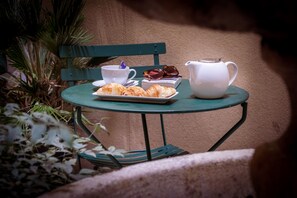 A table with croissants, a teapot, and a cup, set against a green chair and a beige wall. - Hotel Saint Honore 85 (Paris)