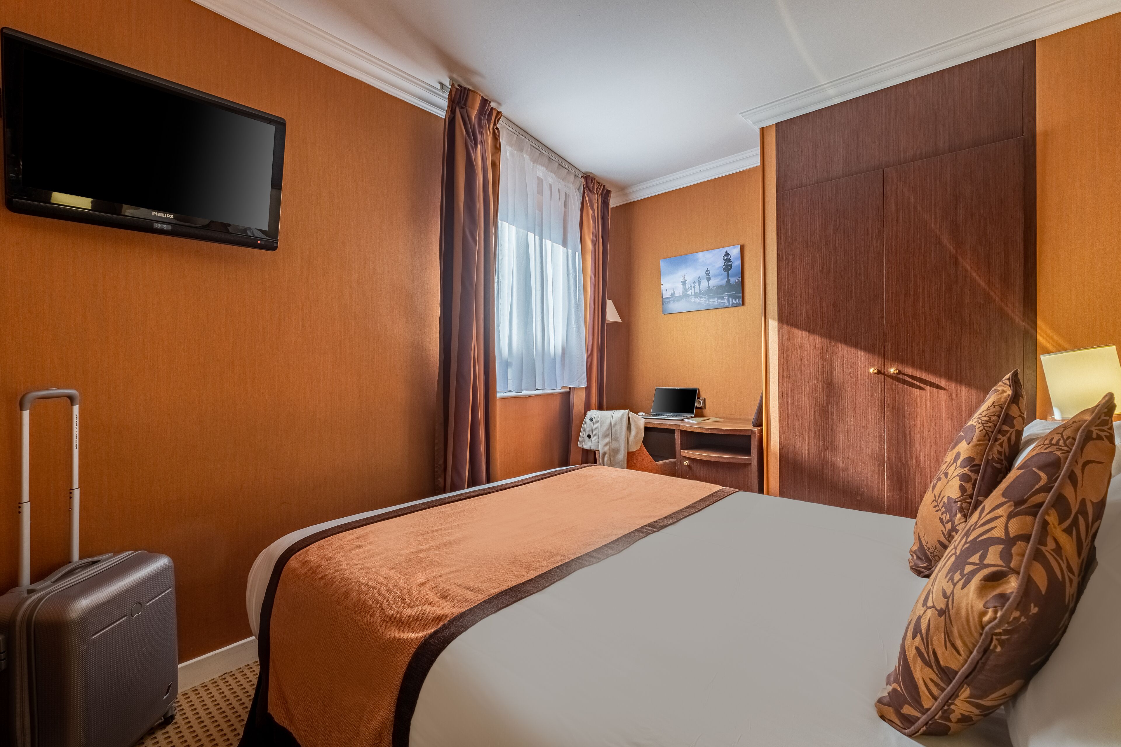 Een hotelkamer met een bed, een bureau met een laptop, een televisie en een koffer.