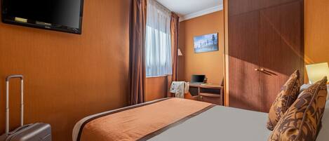 A hotel room with a bed, a desk with a laptop, a television, and a suitcase.