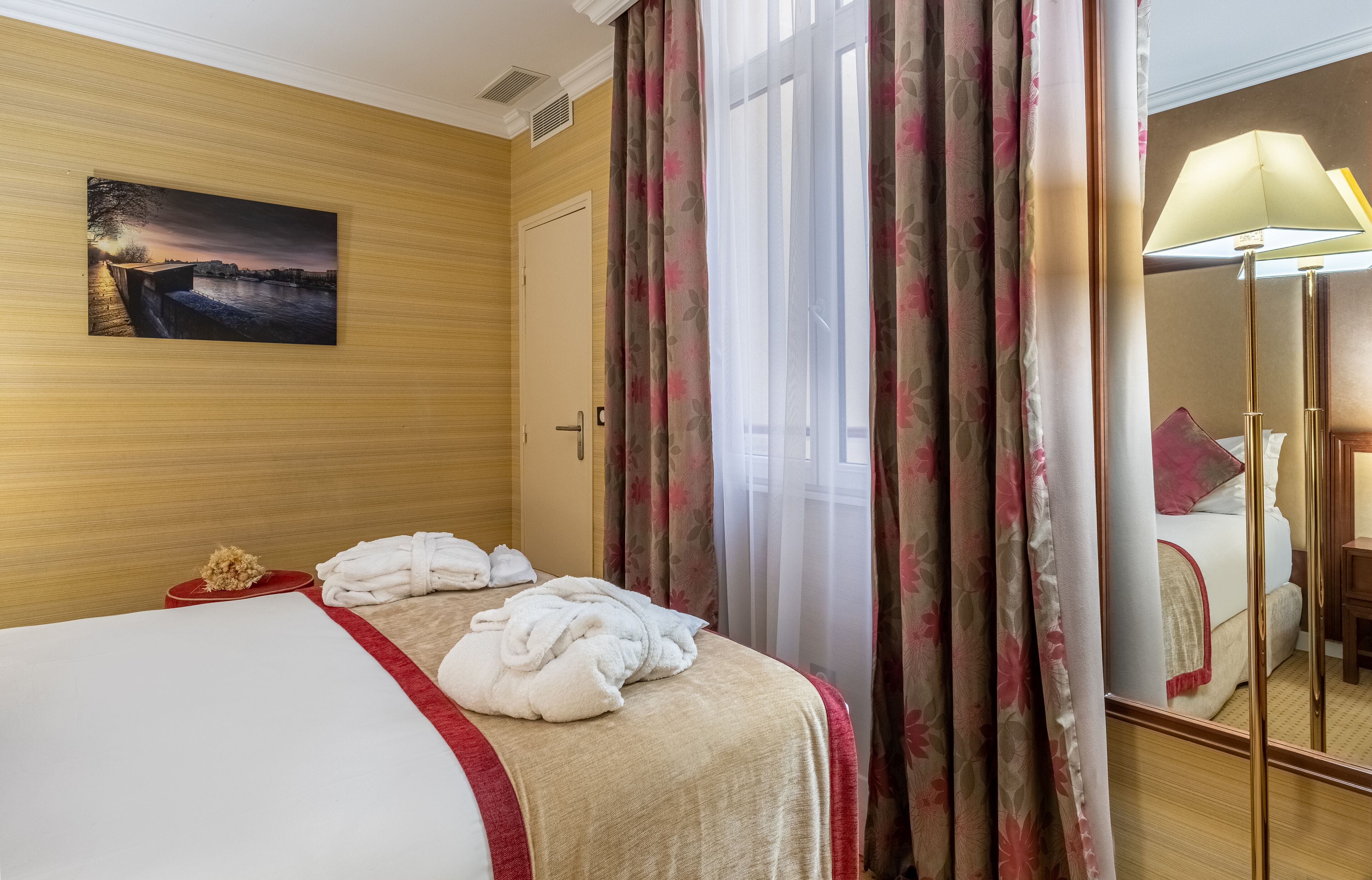 A hotel room with a bed, a painting on the wall, and a window with curtains.