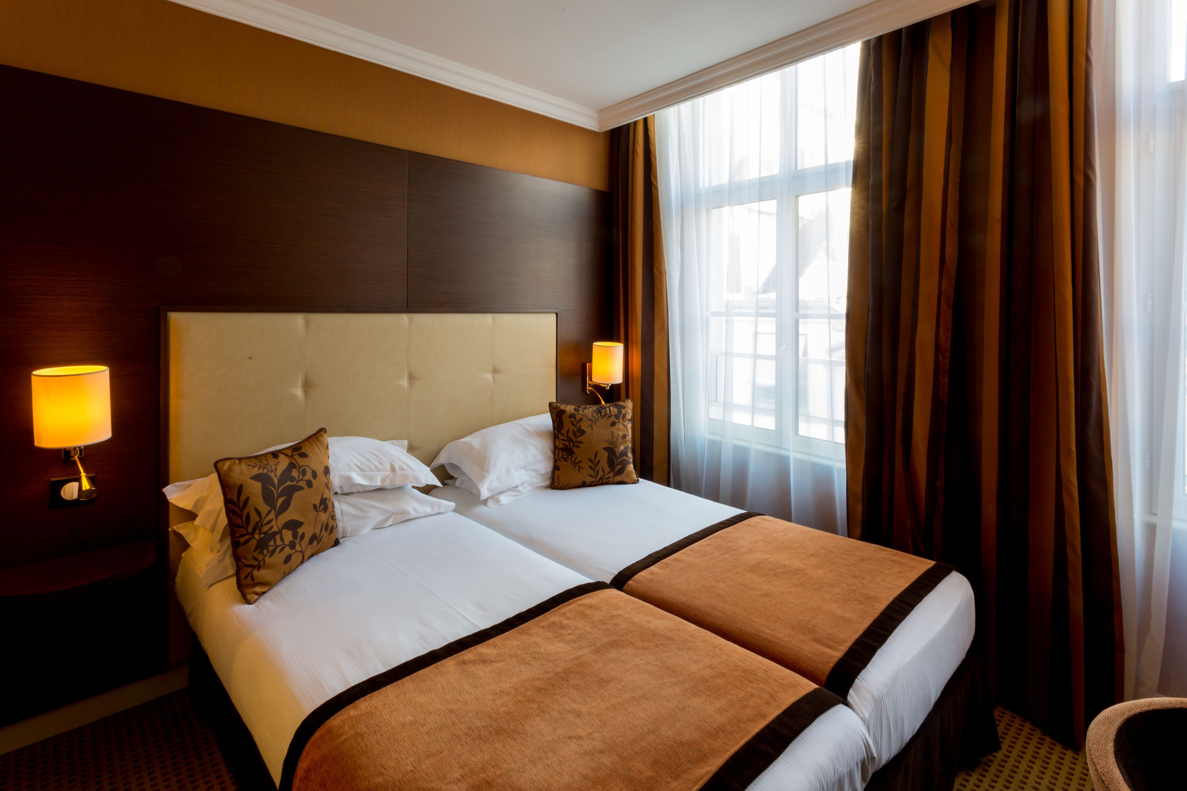 A hotel room with a large bed, two bedside lamps, and a window with curtains.