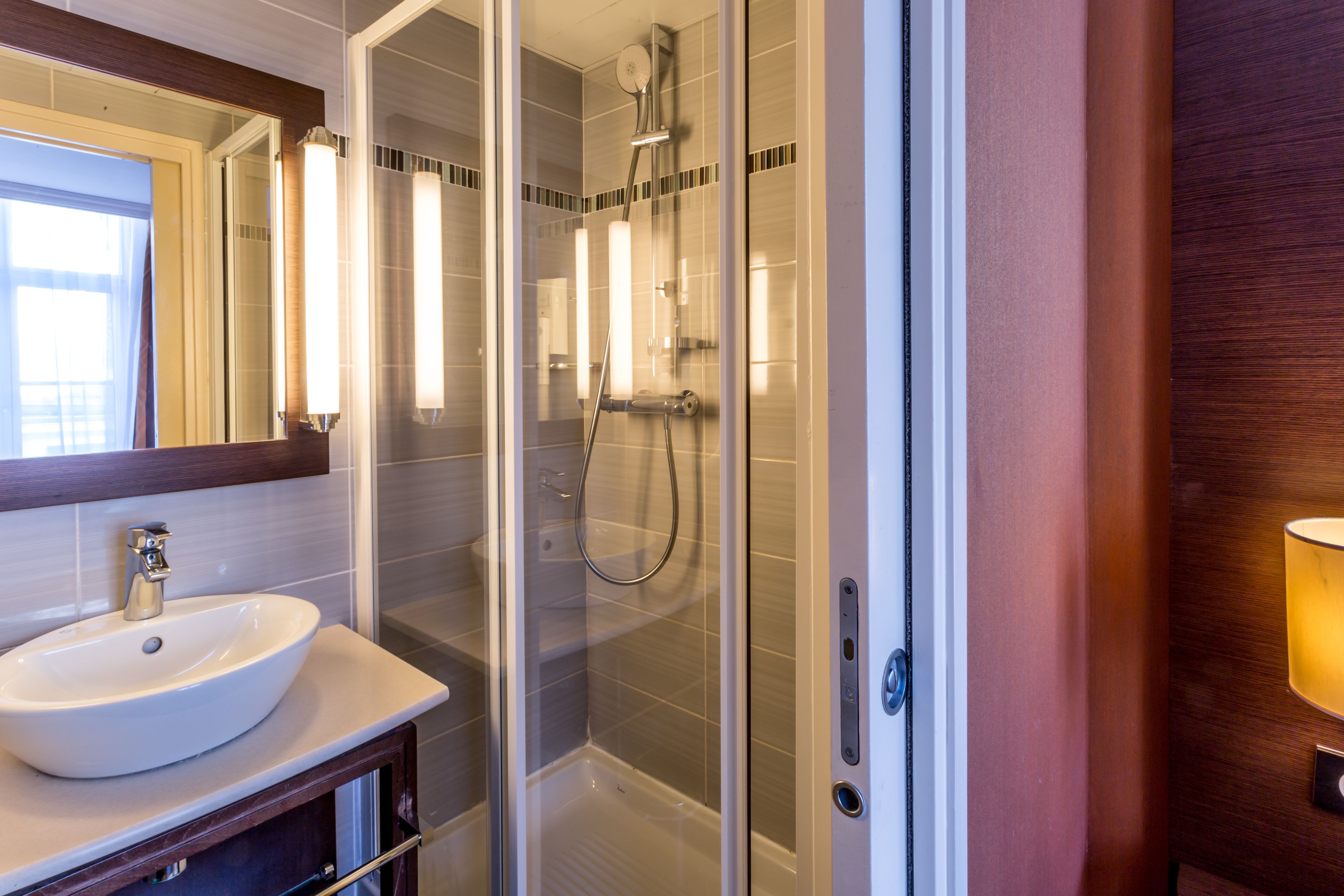 A modern bathroom with a glass-enclosed shower, a white sink, and a mirror above it.