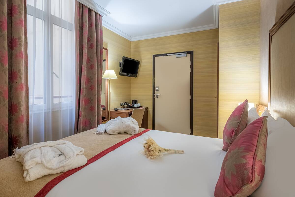A hotel room with a bed, a TV mounted on the wall, a desk with a chair, and a door.
