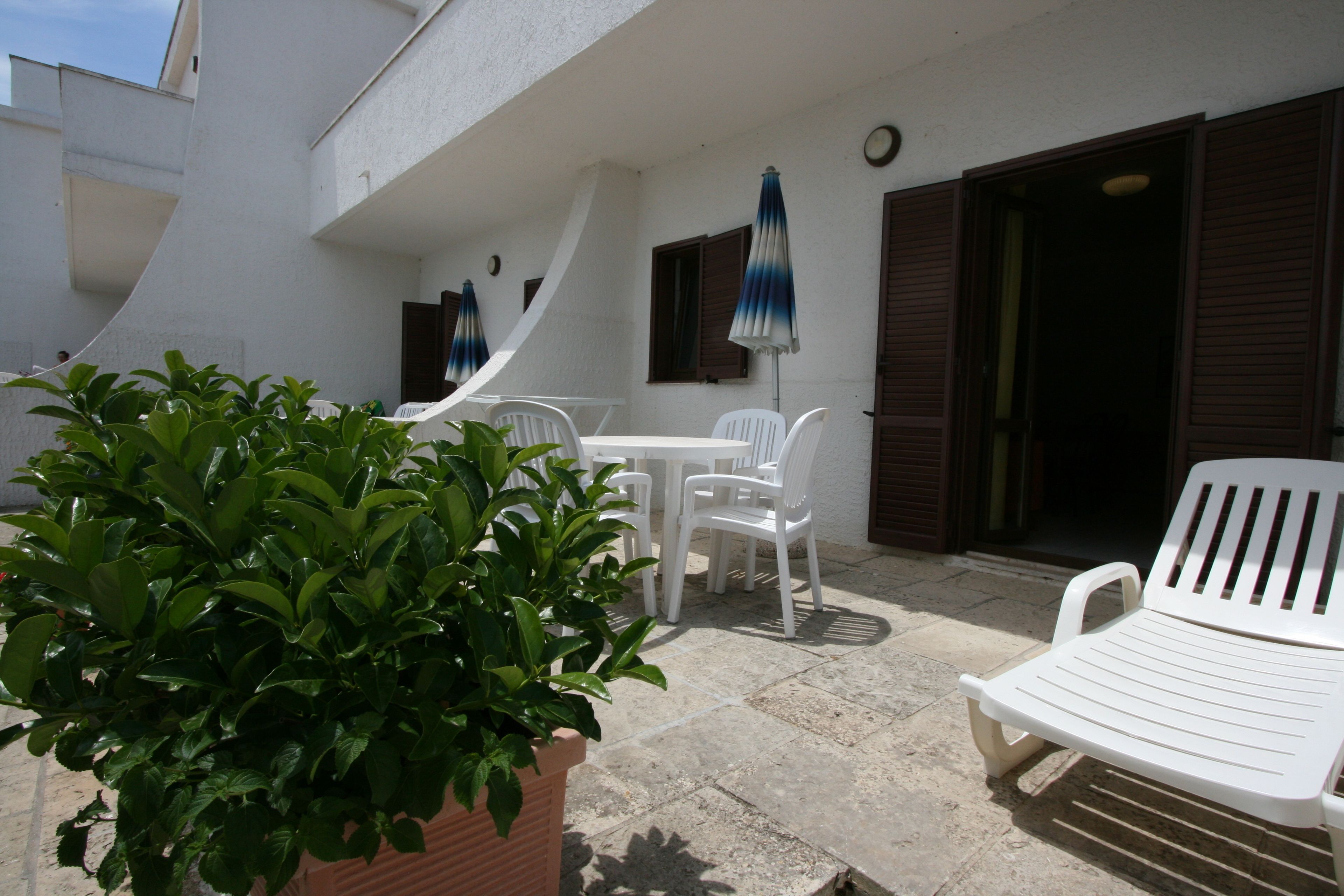 Un espace patio avec des chaises et une table en plastique blanc, entouré de plantes en pot.