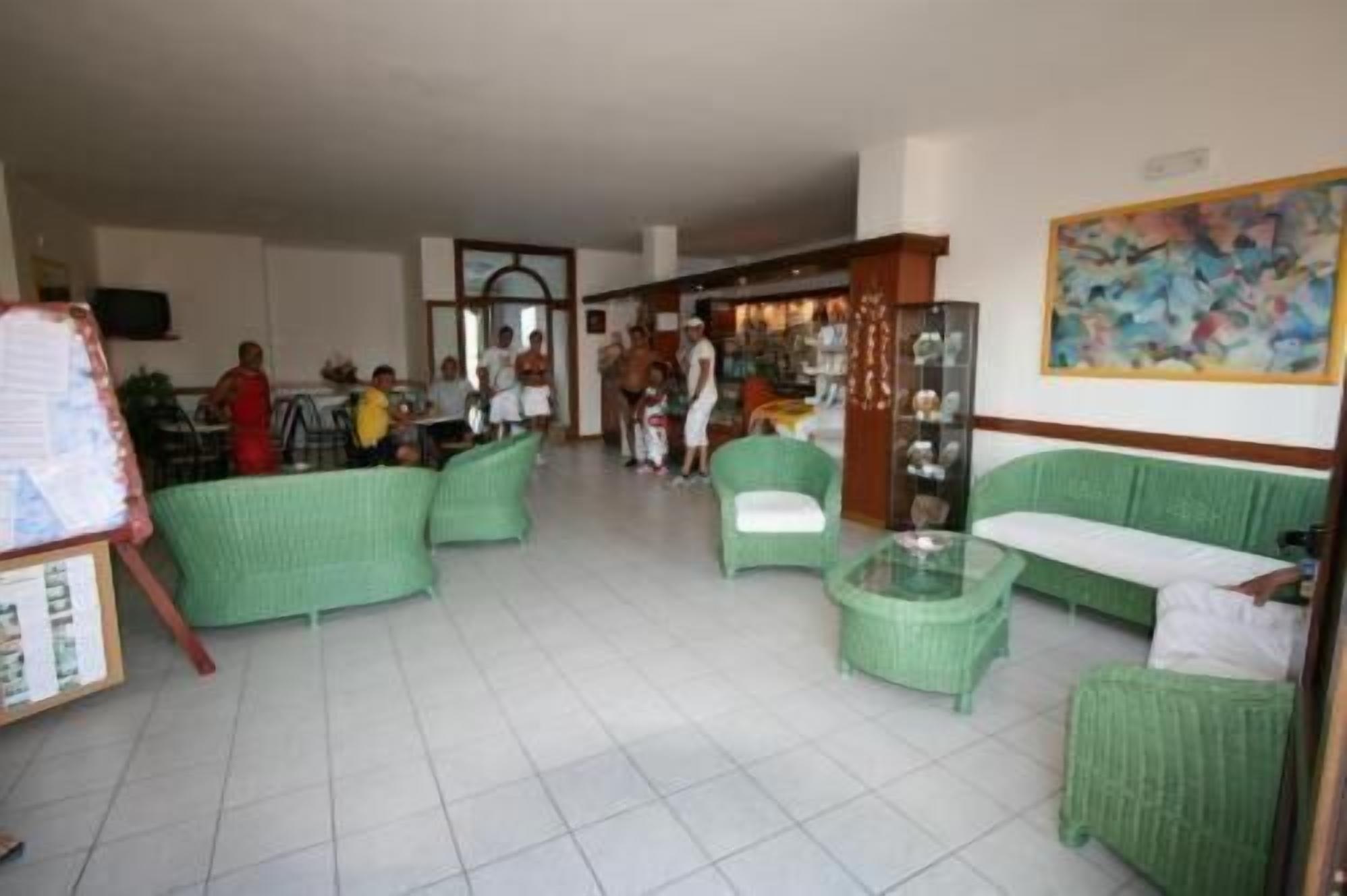 A spacious living area with green upholstered furniture, a glass coffee table, and a painting on the wall.