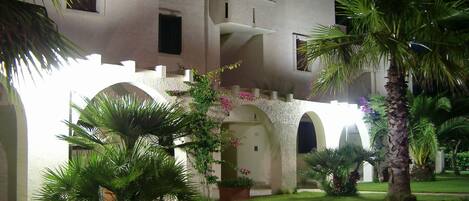A building with multiple arches and a well-maintained garden with palm trees and flowers.
