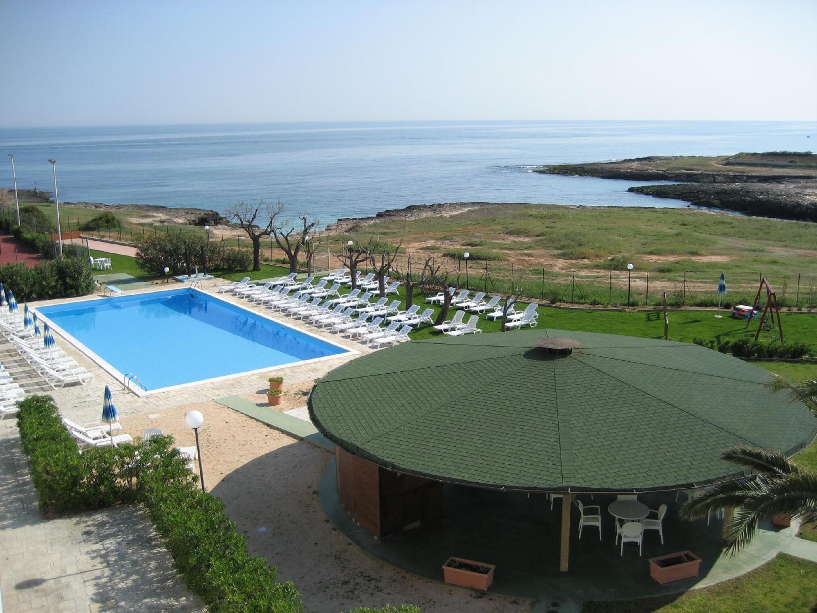 Una piscina con lettini, una zona relax all'aperto coperta e vista sul mare.