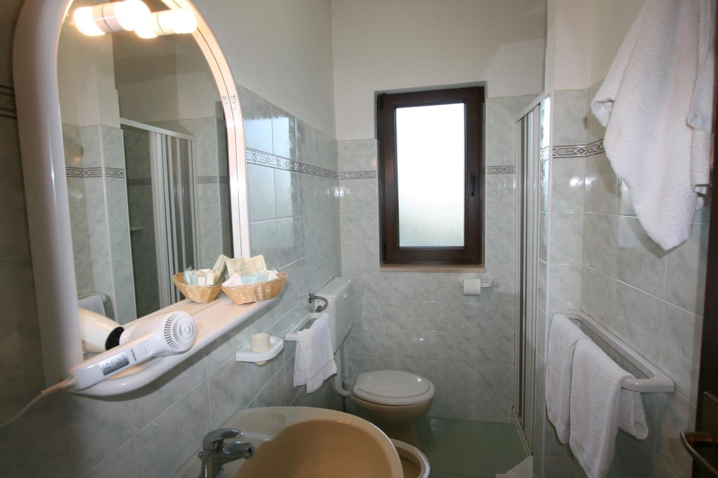 Ein Badezimmer mit großem Spiegel, Föhn, Waschbecken, Toilette und Duschbereich.