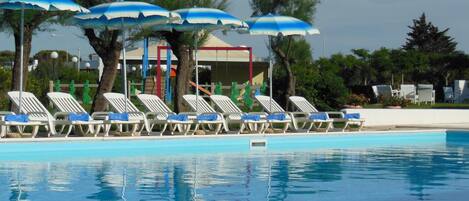 Une piscine avec des chaises longues et des parasols bleus.