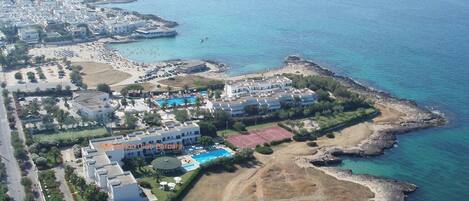 Vista aèria d'un hotel costaner amb diversos edificis, una piscina i un litoral rocos.