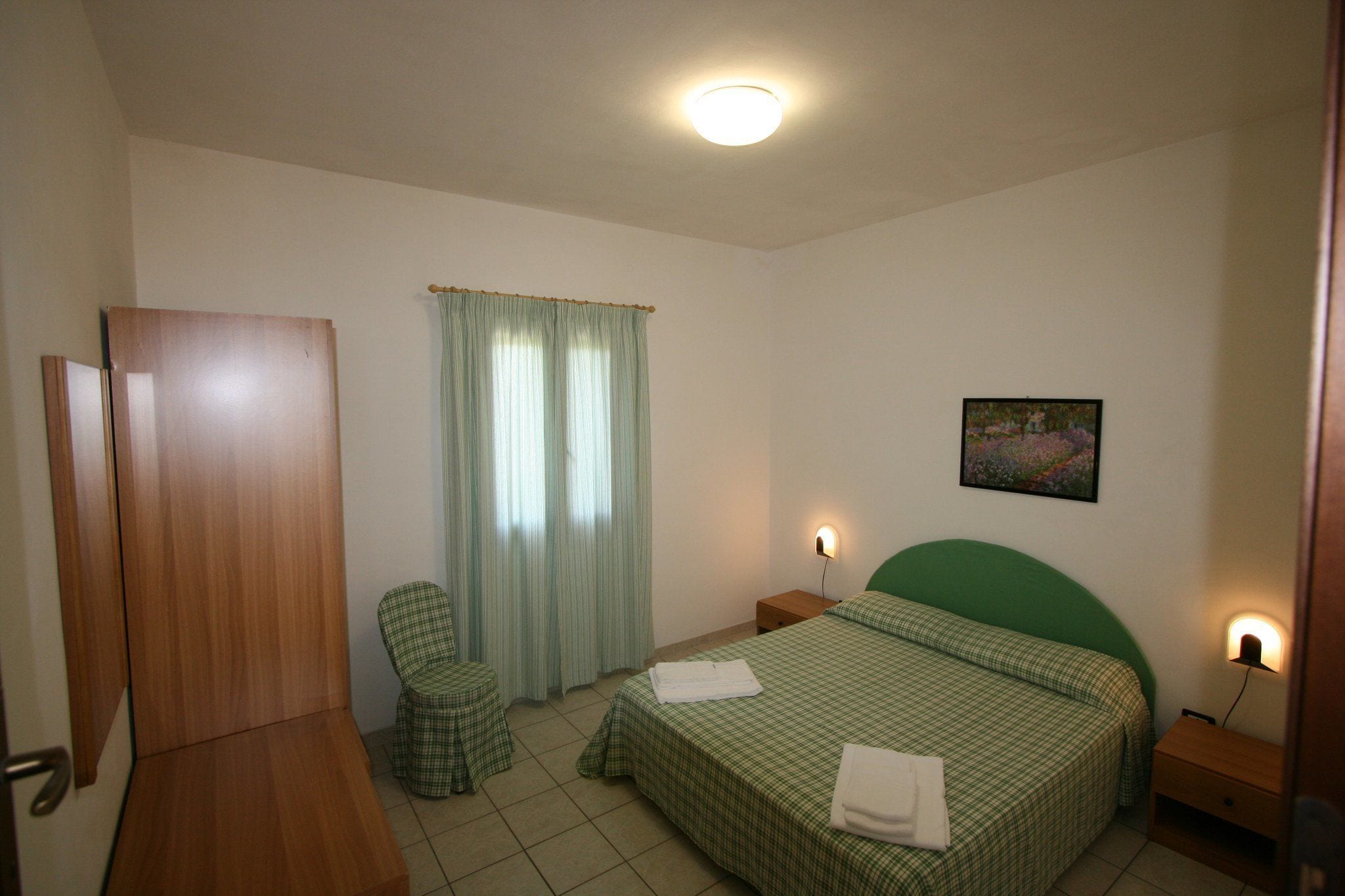 Ein Schlafzimmer mit einem Bett, einem Sessel, einem Nachttisch, einem Wandbild und einer Tür.