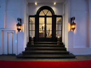 A grand entrance with a black door, a red carpet, and two wall-mounted lanterns. - Patritius (Bruges)