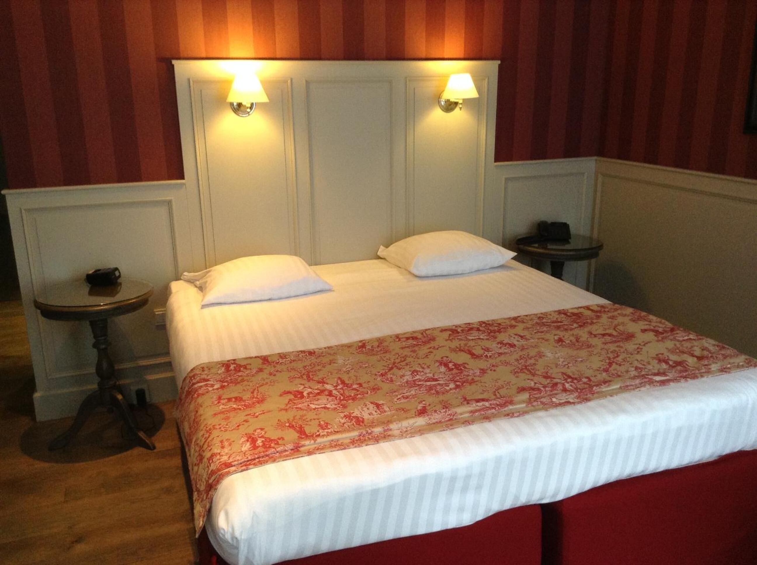 A neatly made bed with a floral bedspread, two bedside lamps, and a small table with a telephone on each side.