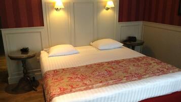 A neatly made bed with a floral bedspread, two bedside lamps, and a small table with a telephone on each side.