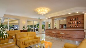 Amplia sala de estar con sofás amarillos, una mesa de centro de vidrio y una zona de bar con mostrador y taburetes de madera.
