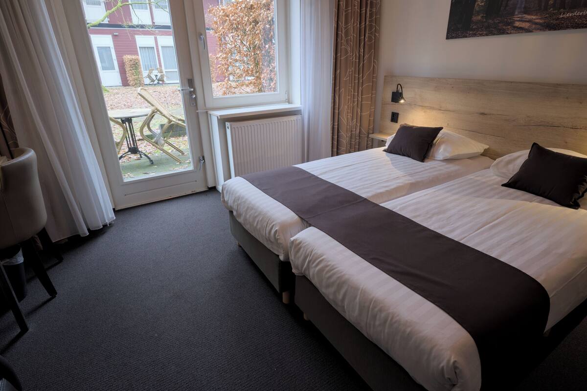 A hotel room with a large bed, a wooden headboard, a window with curtains, and a view of the outside.