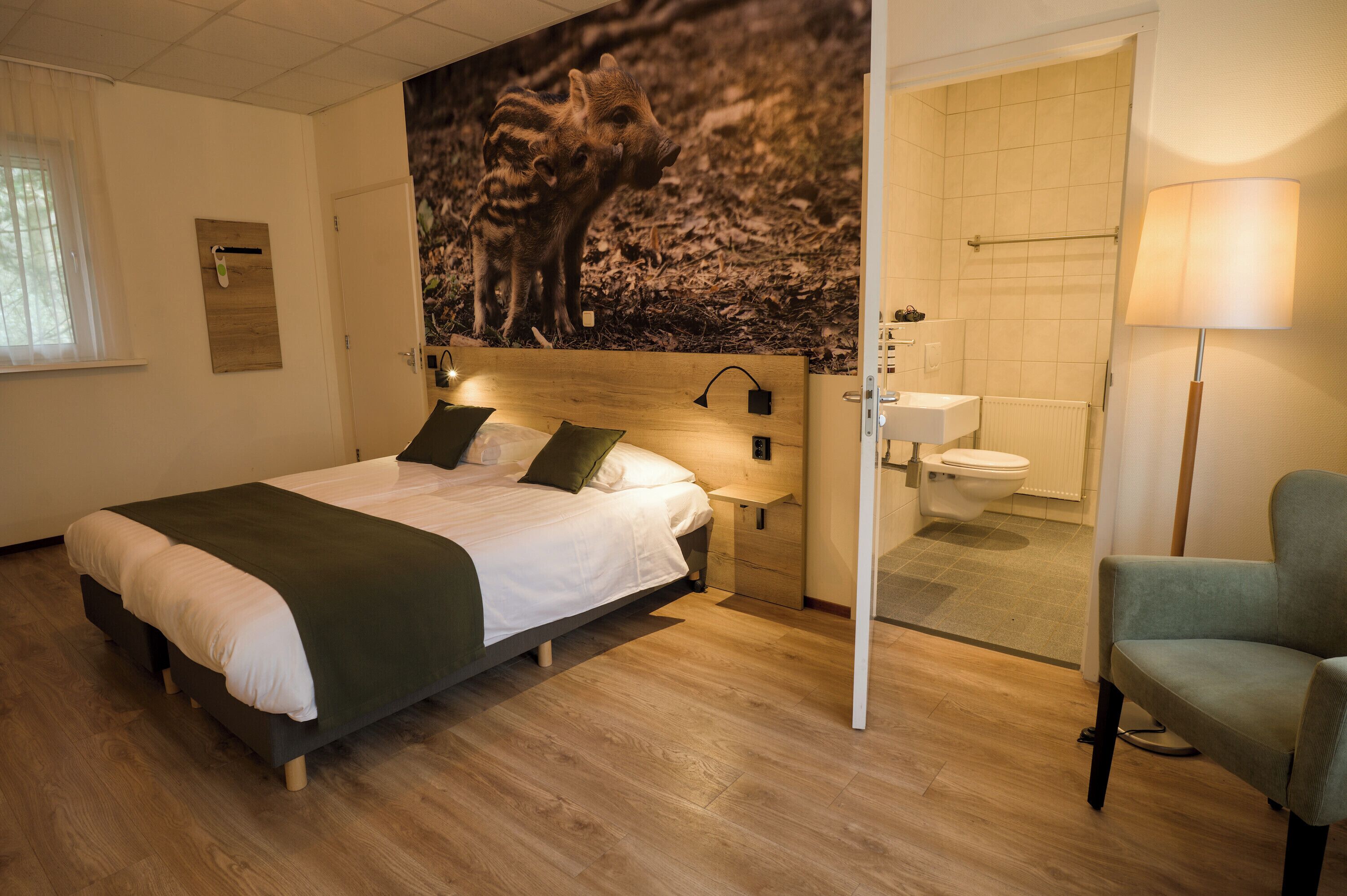 Hotelkamer met een bed, nachtkastje, lamp, stoel, badkamer met toilet en wastafel, en een wandplank.
